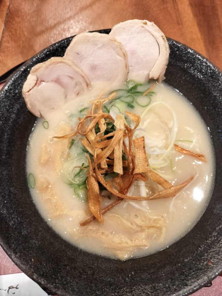 A bowl of ramen with green onions, chashu braised pork, dried crispy fish flakes and a rich broth.  
(This is from when I lived in Japan)